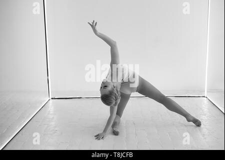 Graziosa ginnasta nel corpo collant su uno sfondo bianco fa di forme complesse.Sport, ginnastica, stretching. Foto Stock