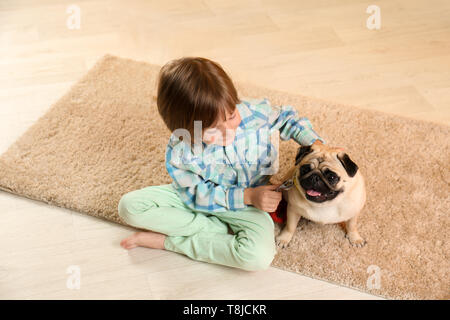 Piccolo Ragazzo seduto con cute pug cane sul pavimento a casa Foto Stock