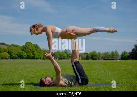 Atletica Giovane coppia innamorata di eseguire acro yoga in Roath Park su una luminosa giornata di sole. Foto Stock