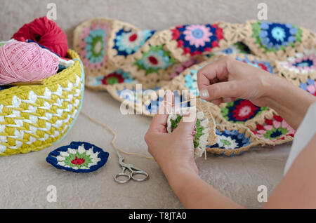 There are multi colored yarns in a basket  front of  to the woman.  The woman is crocheting  baby blanket with multi colored yarns Foto Stock