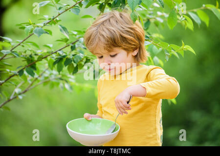 Nutrizione organica. Nutrizione sana nozione. Abitudini alimentari. Kid tenere cucchiaio. Piccolo bambino di gustare pasti fatti in casa. La nutrizione per i bambini. Poco toddler boy porridge di mangiare all'aperto. Avendo grande appetito. Foto Stock