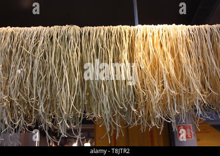 Gustosa la pasta fresca con filamenti simili preparata di fresco e impastati gli spaghetti e disposti in una fila su un filo per asciugare Foto Stock