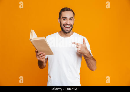 Immagine dell uomo unshaved 30s in t-shirt bianco holding e la lettura prenota isolate su sfondo giallo Foto Stock