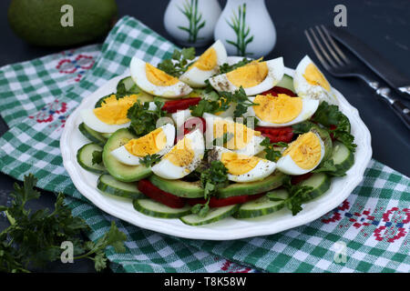 Una sana insalata di avocado, cetrioli, uova e pepe dolce situato in una piastra su sfondo scuro Foto Stock