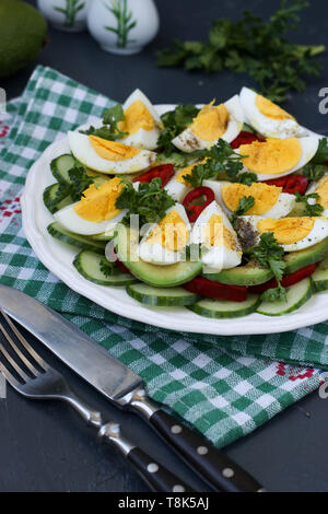 Utile insalata di avocado, cetrioli, uova e pepe dolce situato in una piastra contro uno sfondo scuro, foto verticale Foto Stock