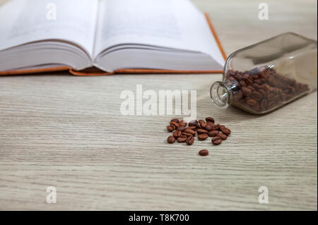 Close-up. Libro aperto su un tavolo bianco e una bottiglia di chicchi di caffè, il concetto di istruzione Foto Stock