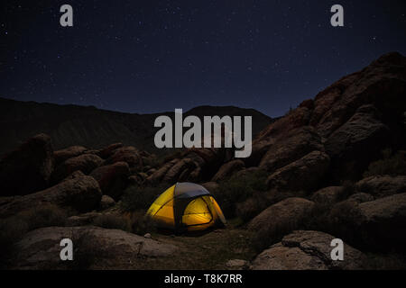 Illuminato tenda istituito tra rocce di notte sotto un cielo stellato Foto Stock