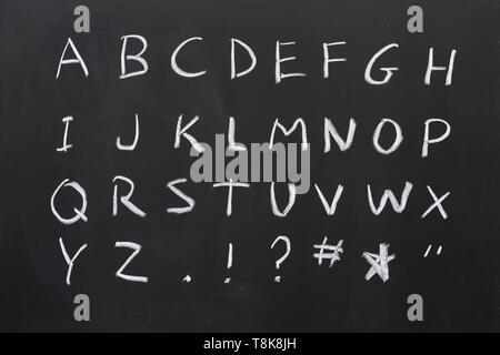 Alfabeto di capitale scritto in bianco gesso su una lavagna con alcuni simboli Foto Stock