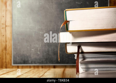 Vista ravvicinata della pila di libri su un tavolo di legno con blackboard sfondo. Si torna a scuola concept Foto Stock