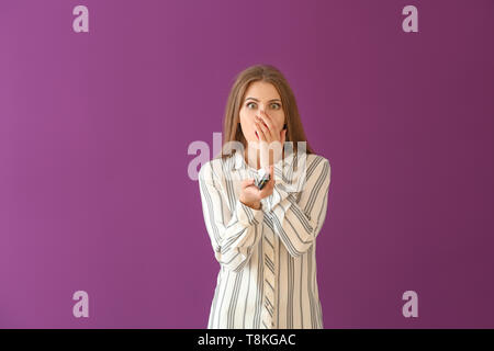 Emotional giovane donna con il comando remoto sul colore di sfondo Foto Stock