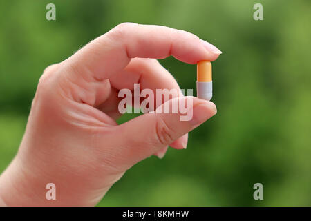 Il farmaco in capsule in mano femmina su sfocata natura verde dello sfondo. Concetto di vitamine per la bellezza, la dieta pillola, health care, farmaco naturale Foto Stock