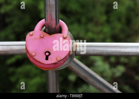 Vecchio lucchetto rosa a forma di cuore su un ponte. Simbolo dell'amore eterno in un parco verde sullo sfondo della natura Foto Stock