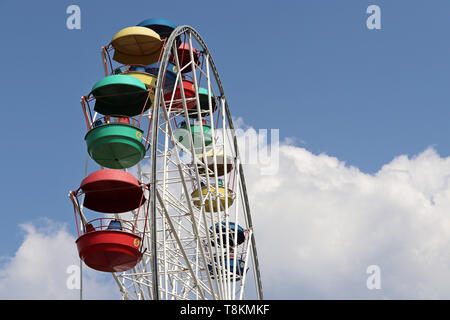 Ruota panoramica con cabine colorati contro il cielo blu e nuvole bianche. La gente ride damn ruota nel parco di divertimenti Foto Stock