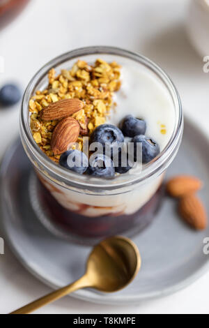 Close up granola con mandorla, marmellata, yogurt e mirtillo in vaso, su lastra grigia. Concetto di una sana prima colazione. Sfondo per il testo Foto Stock