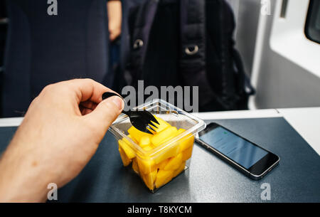 Uomo di mangiare in treno insalata di anguria con la forcella - viaggi in treno veloce nel Regno Unito lo smartphone piccolo sul tavolo Foto Stock