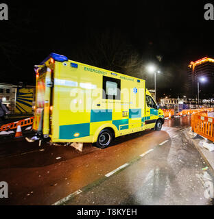 London, Regno Unito - Mar 5, 2017: Giallo NHS Ambulance guida veloce sul riparato con lavori stradali street nel centro di Londra di notte immagine quadrata Foto Stock