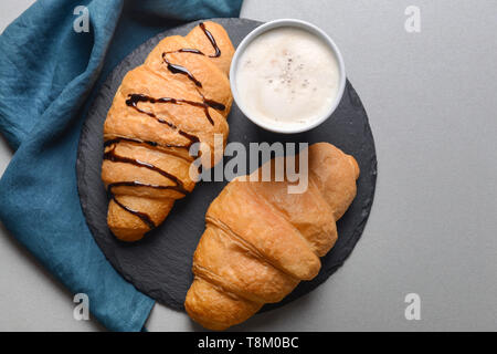 Piastra di ardesia con cornetti e tazza di bevanda su sfondo grigio Foto Stock