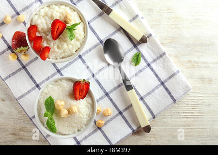 Delizioso budino di riso con fragole e nocciole in ciotole sul tavolo Foto Stock