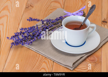 Il tè in una tazza bianca e un mazzetto di lavanda essiccata su un tovagliolo di lino close-up Foto Stock