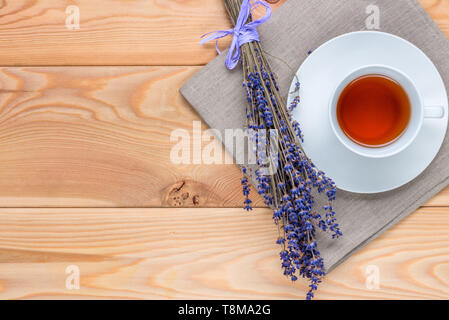 Vista superiore tazza di tè rilassanti con lavanda e un mazzo di fiori su un tovagliolo di lino su assi di legno Foto Stock