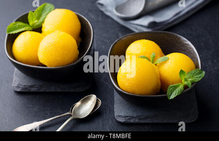 Gelato al mango tropicale sorbetto di frutta in vaso nero su sfondo di ardesia. Foto Stock