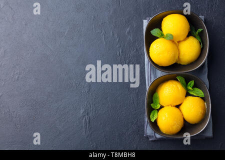 Gelato al mango tropicale sorbetto di frutta in vaso nero su sfondo di ardesia. Copia dello spazio. Vista dall'alto. Foto Stock