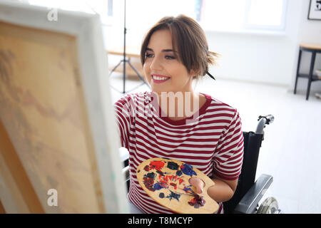 Giovane artista femminile nella pittura di sedia a rotelle foto a casa Foto Stock