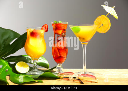 Estate freschi cocktail in bicchieri con foglia tropicale sul tavolo di legno contro uno sfondo grigio Foto Stock