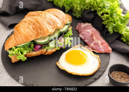 Croissant gustosi sandwich con uovo fritto sulla piastra di ardesia Foto Stock