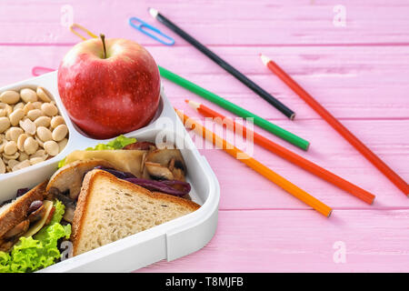 Scatola di pranzo con cibo appetitoso e articoli di cancelleria sul colore tavolo in legno Foto Stock