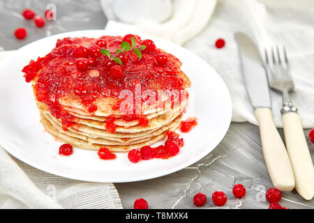 American pancake con la marmellata - berry, pallon di maggio, mirtillo rosso su sfondo grigio. Pancake fatti in casa con salsa di frutti di bosco e le foglie di menta. Sana colazione con prodotti freschi h Foto Stock