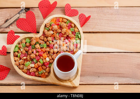 Colorata frutta secca in un vassoio a forma di cuore con tè Foto Stock