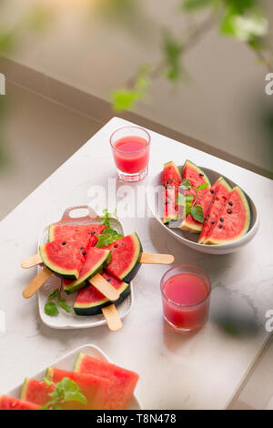 Fresco frullato di rosso in un bicchiere con pezzi tagliati a fette di cocomero sul tavolo. Foto Stock