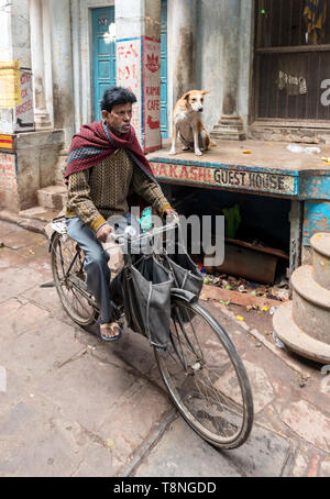Uomo in bicicletta nelle stradine della città vecchia di Varanasi, India Foto Stock