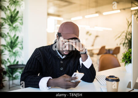 Bello stanco Afro American businessman in abiti casual è il massaggio ponte nasale mentre si lavora con un portatile a casa Foto Stock