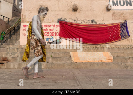 Sadhu (uomo santo) coperto di cenere passeggiate lungo i ghats del Fiume Gange, Vranasi, India Foto Stock