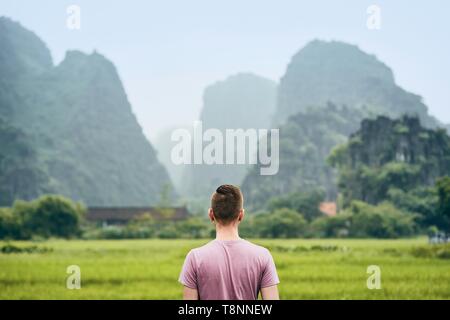 Traveler in Vietnam. Vista posteriore del giovane uomo contro colline carsiche vicino Tam Coc in Ninh Binh provincia. Foto Stock