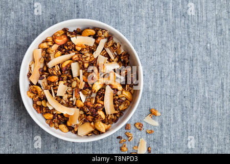 Il Granola fresca, muesli con noce di cocco, banani e i dadi in una ciotola bianco su sfondo grigio. Copia dello spazio. Vista dall'alto. Foto Stock