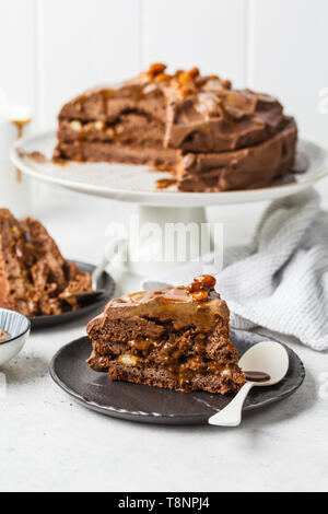 Pezzo di fatti in casa torta al cioccolato con crema di cioccolato su un piattino nero, sfondo bianco. Foto Stock