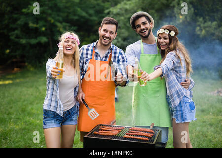 Coppia giovane con amici sorrisi e fare barbecue arrosto in campeggio Foto Stock