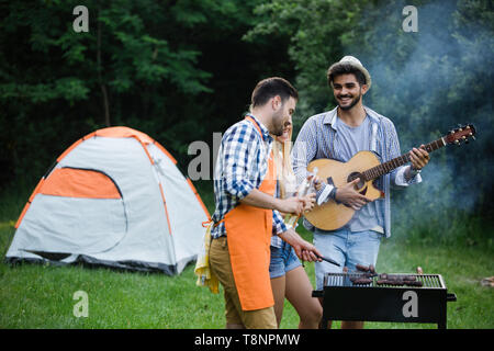 Gruppo di persone felici intorno permanente grill, chat, bere e mangiare. Foto Stock