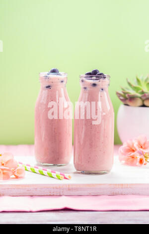 Rosa milk shake in bottiglie di vetro e rabboccato con mirtilli. Fiori di colore rosa e cannucce colorate. Foto Stock