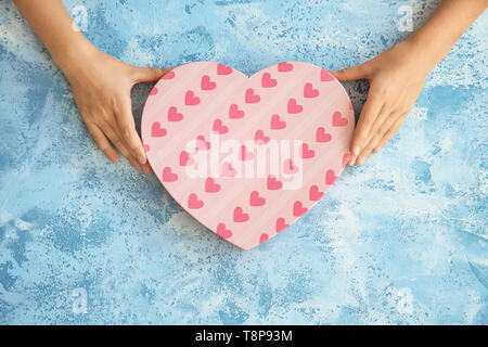 Le mani del bambino tenendo a forma di cuore scatola regalo su uno sfondo colorato Foto Stock