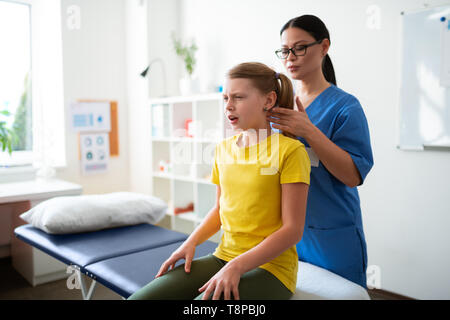 Serio esperto dai lunghi capelli massaggio medico sul retro del collo del suo piccolo client Foto Stock