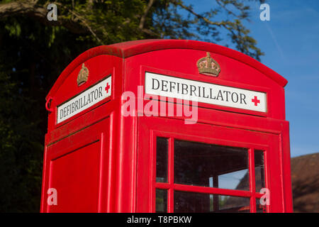 Una tradizionale cassetta telefonica pubblica di colore rosso brillante convertita per ospitare un defibrillatore di emergenza comunitario a Peppard Common, Oxfordshire Foto Stock