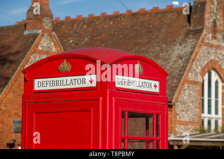 Una tradizionale cassetta telefonica pubblica di colore rosso brillante convertita per ospitare un defibrillatore di emergenza comunitario a Peppard Common, Oxfordshire Foto Stock