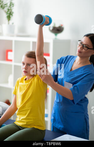 Orgogliosa soddisfatta medico procedura di controllo mentre kid il sollevamento pesi Foto Stock