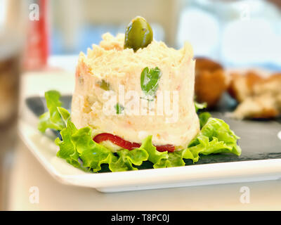 Un 'ensaladilla', uno spagnolo insalata di patate su una piastra bianca guarnita con foglie di lattuga. Il cibo è conformata in una torre rotonda e dispone di un ampio e verde o Foto Stock