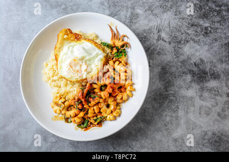 Agitare piccante calamari fritti con foglie di basilico e peperoncino, soleggiato lato fino all'uovo, servito con riso marrone. Piccante e speziato tipico piatto. Foto Stock
