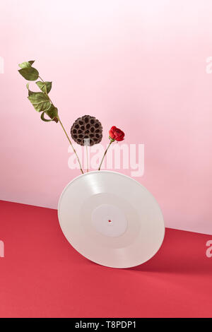 Vinile record retrò decorate con rami secchi e un fiore rosso su una bicromia rosa rosso sfondo con spazio di copia Foto Stock